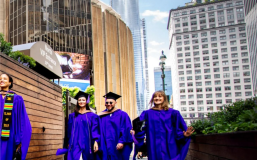 Four students in caps and gowns walking outside